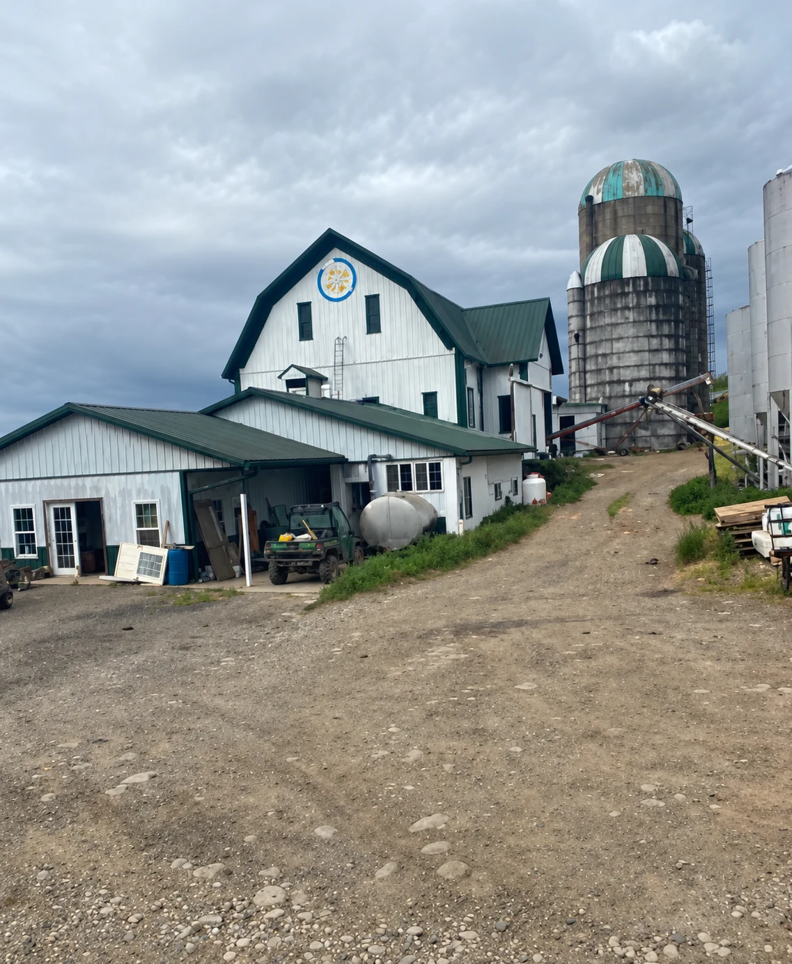 Resolution-enhanced project photo of a white painted barn and green metal roofs beside farm silos